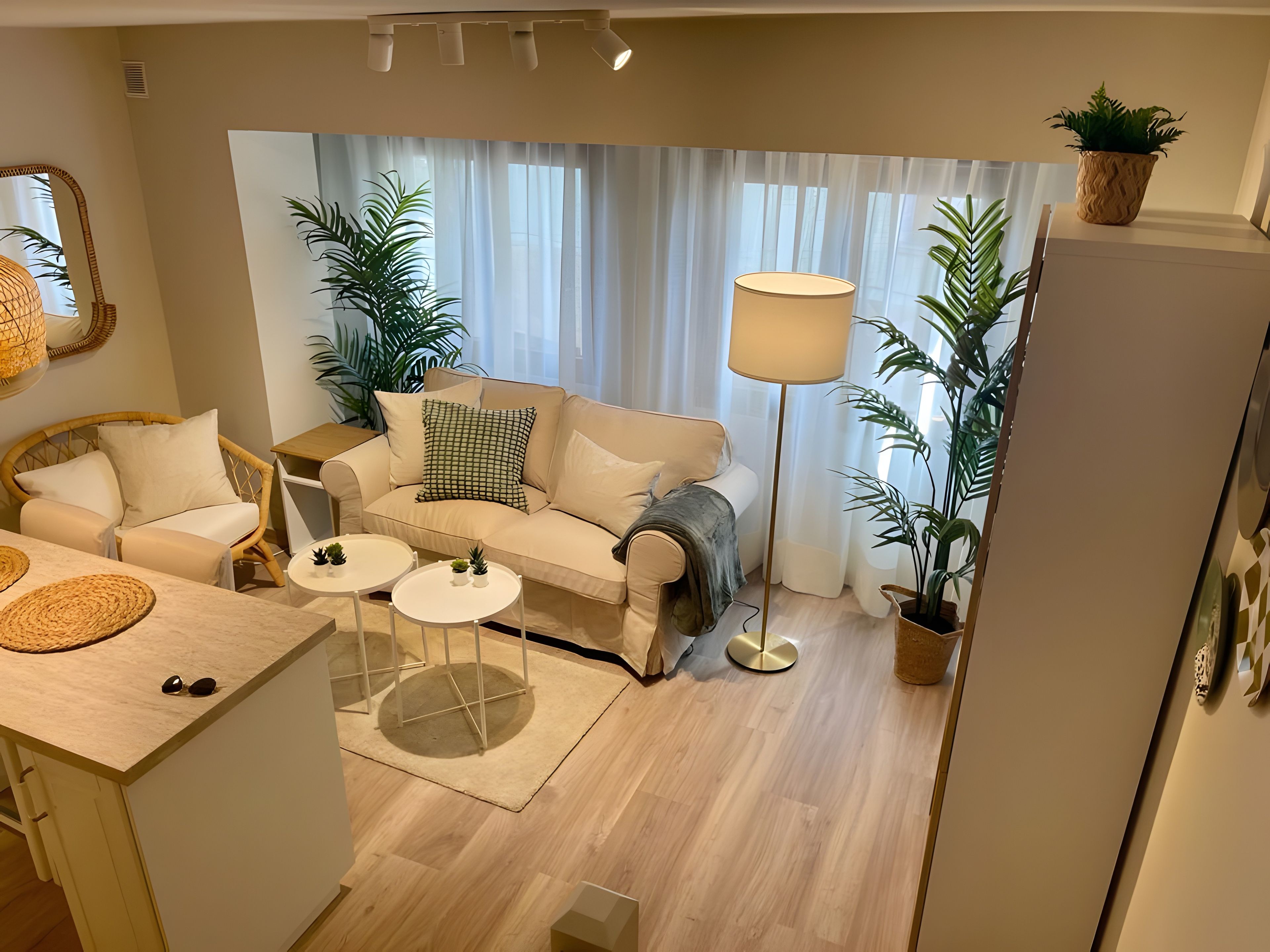 Una sala de estar moderna con un sofá, dos mesitas auxiliares, una lámpara de pie y plantas en macetas.