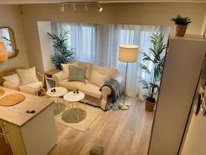 Una sala de estar moderna con un sofá, dos mesitas auxiliares, una lámpara de pie y plantas en macetas.