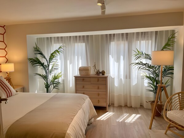 Un dormitorio con una cama, un aparador, una lámpara y dos plantas en macetas.