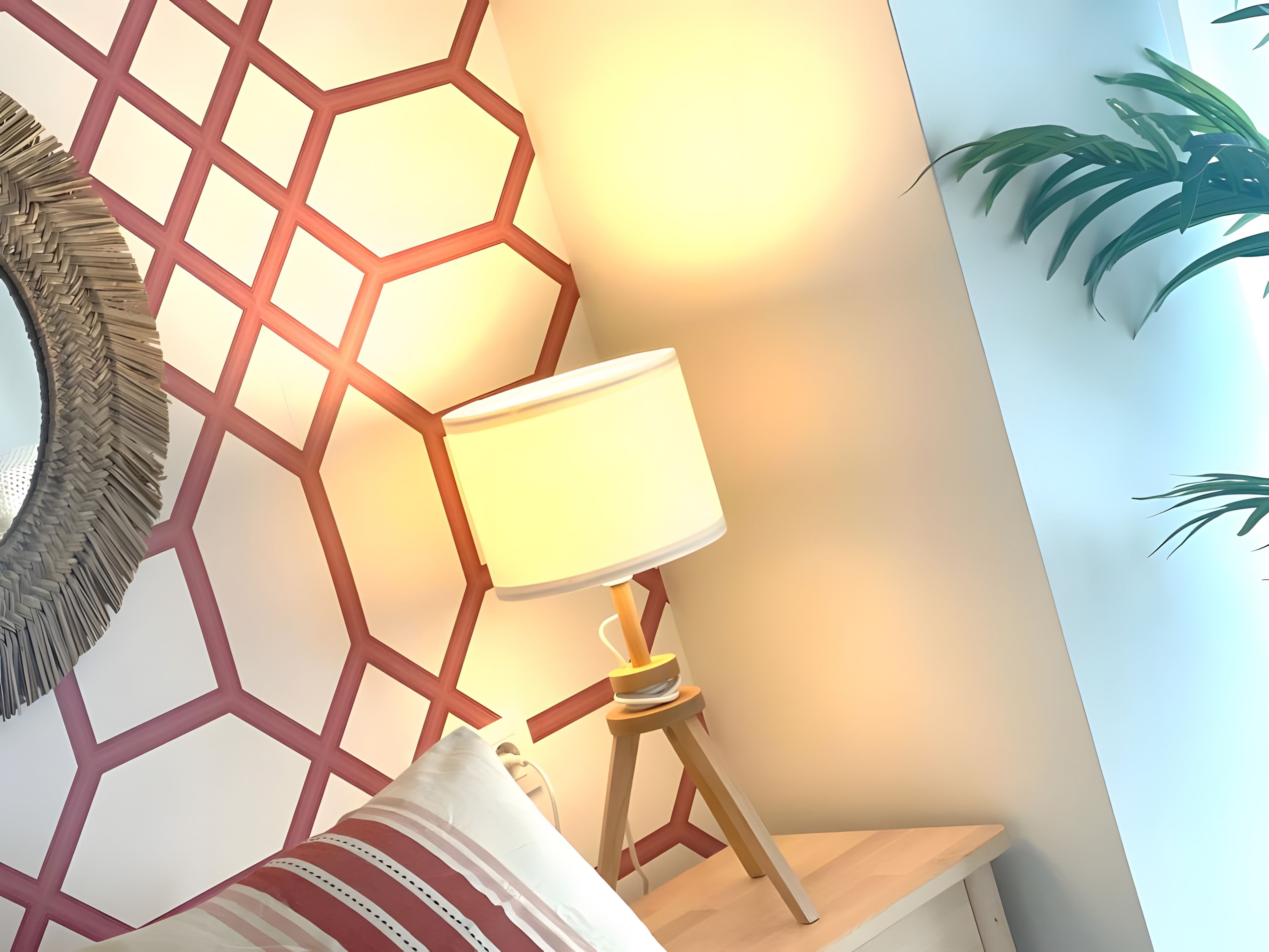 Una habitación con pared de diseño geométrico, una lámpara de noche, un espejo y una planta en maceta.