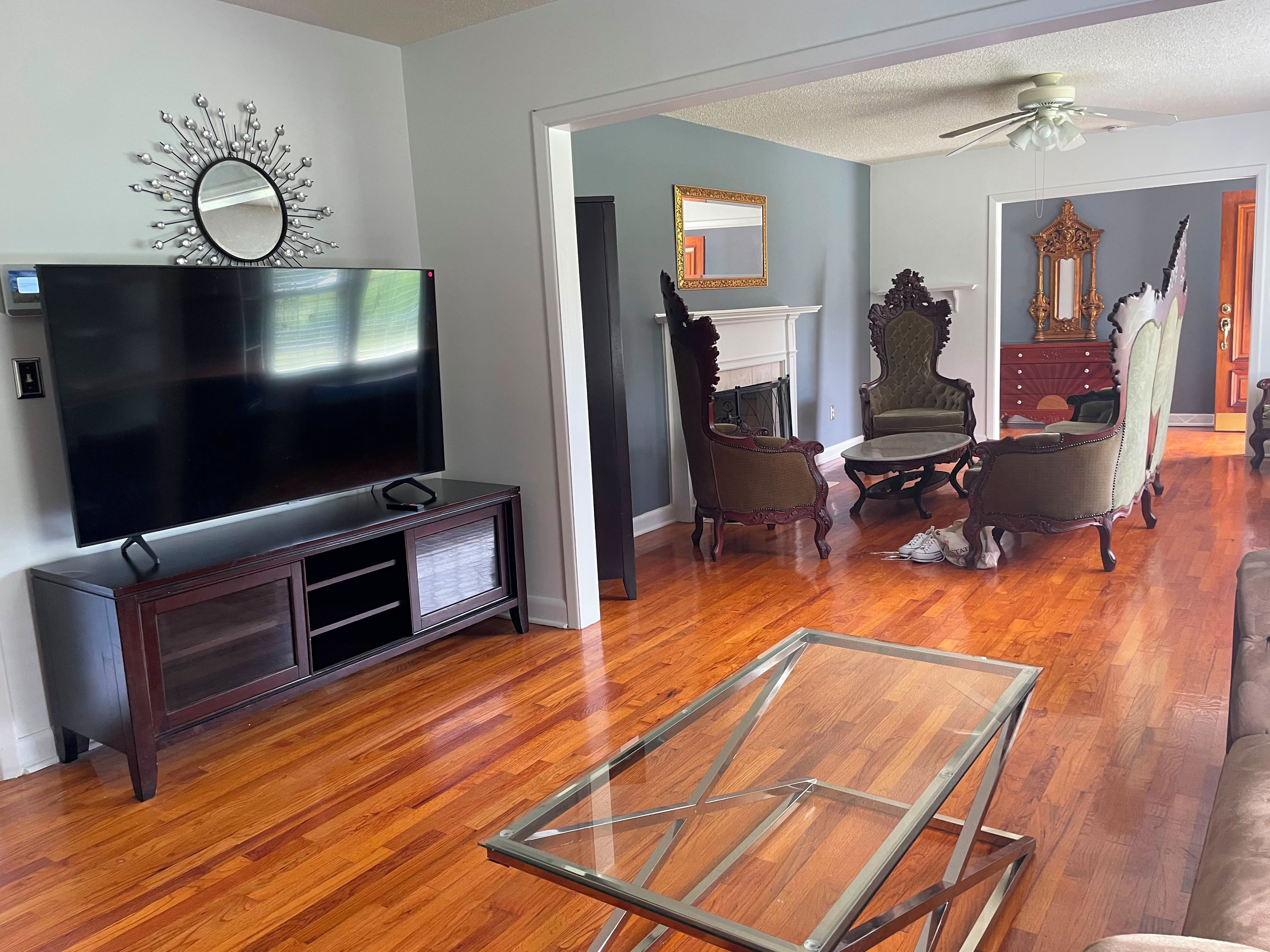 A living room with a flat-screen TV, wooden flooring, a glass coffee table, and vintage furniture.
