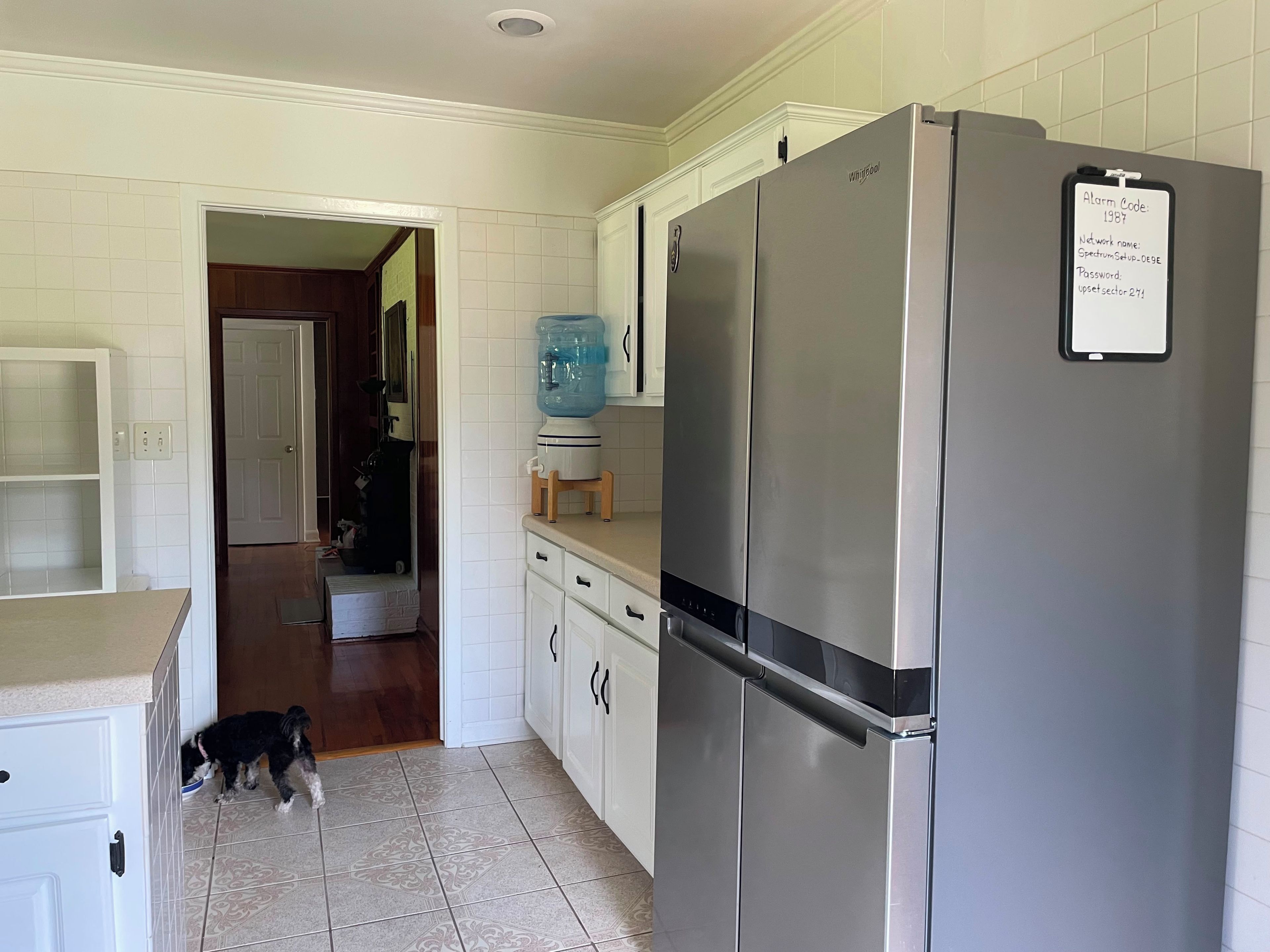 A kitchen with a stainless steel refrigerator, a water dispenser, and a dog near the entrance.