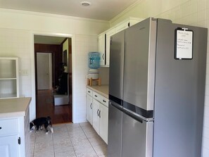 Eine Küche mit einem Edelstahlkühlschrank, einem Wasserspender und einem Hund in der Nähe des Eingangs.