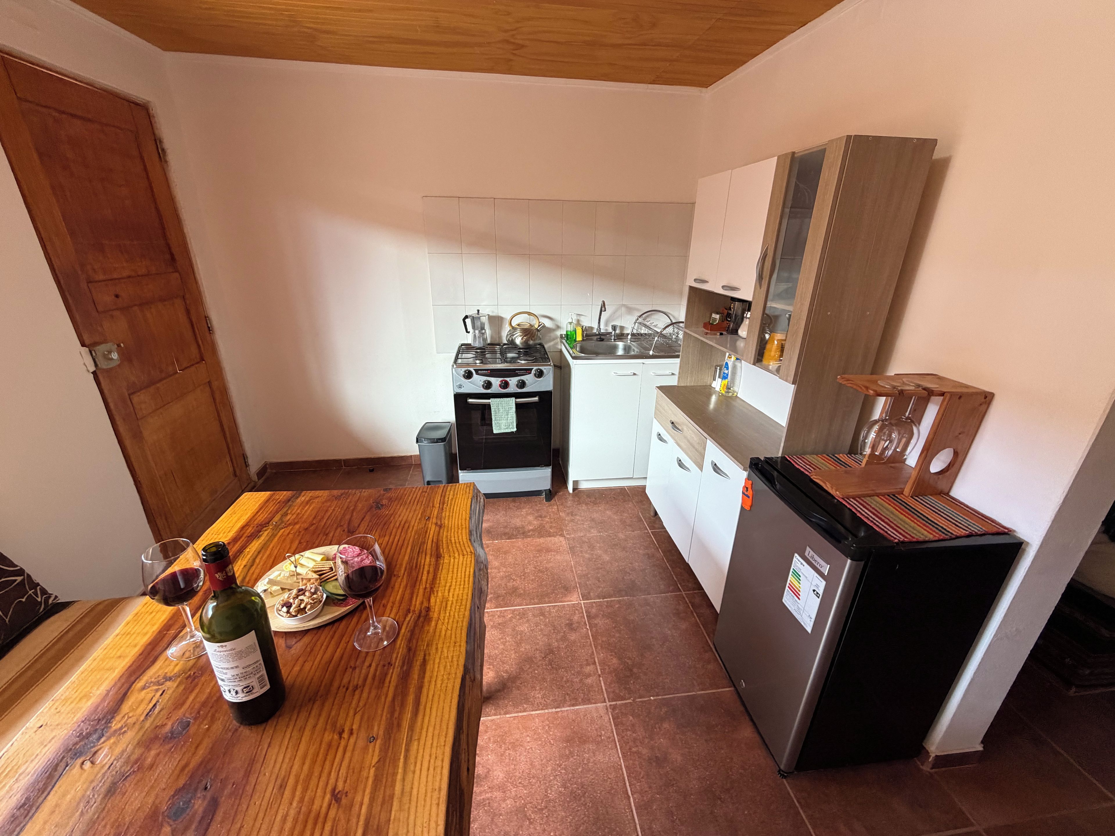Una cocina compacta con una mesa de madera, un refrigerador y una estufa.