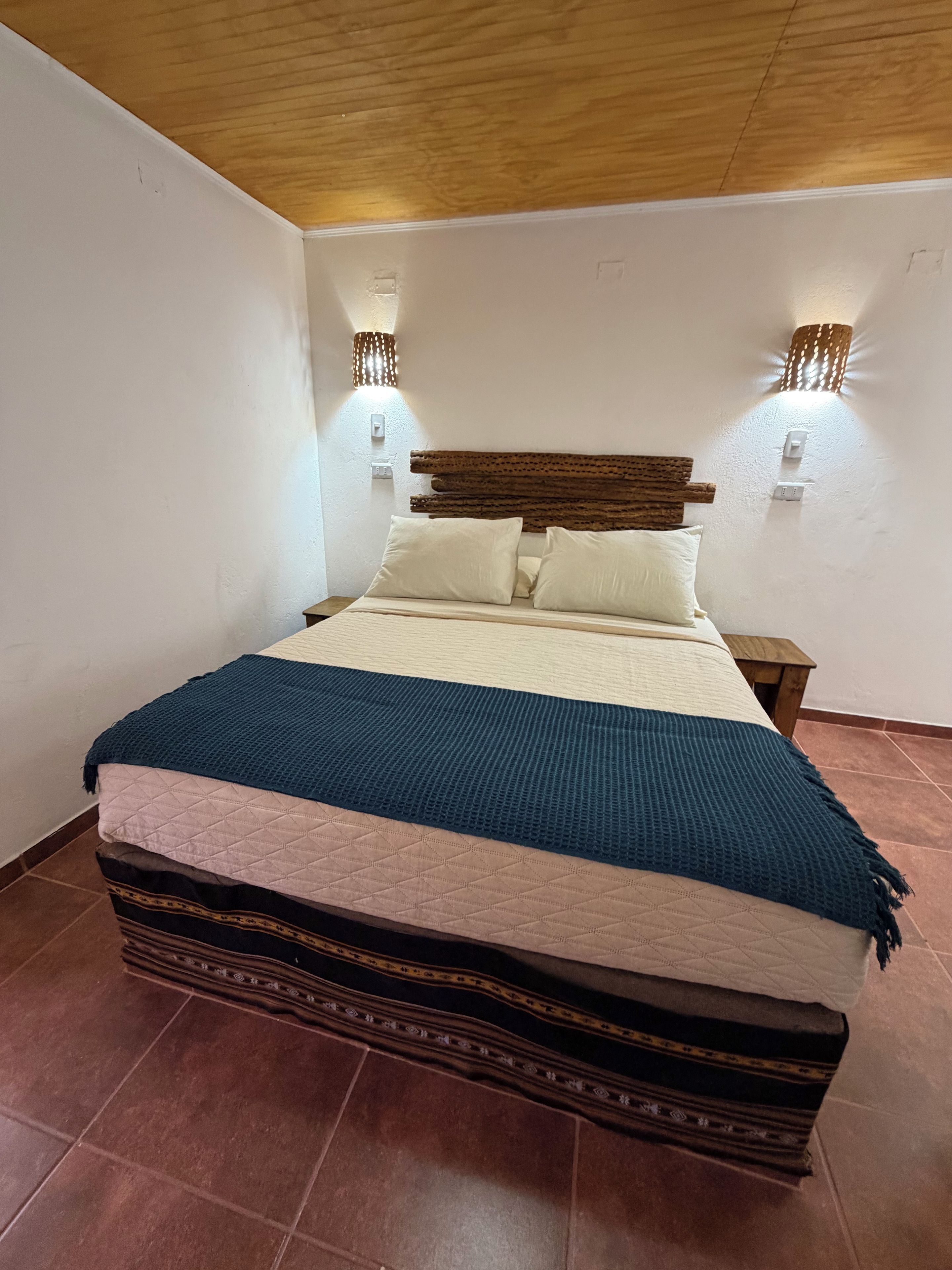Un lit avec une tête de lit, deux lampes fixées au mur et une couverture.