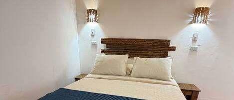 A bed with a headboard, two wall-mounted lights, and a blanket.