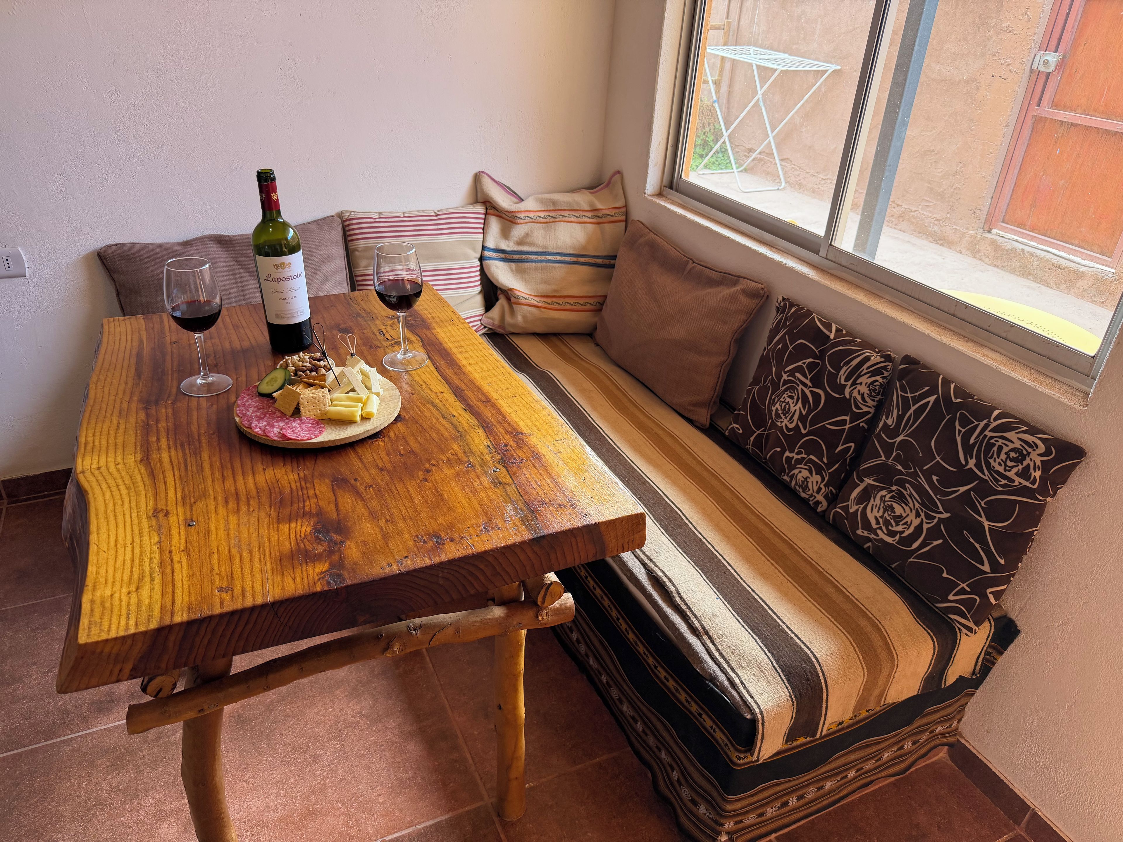 Una mesa de madera con una botella de vino, copas y una tabla de quesos.