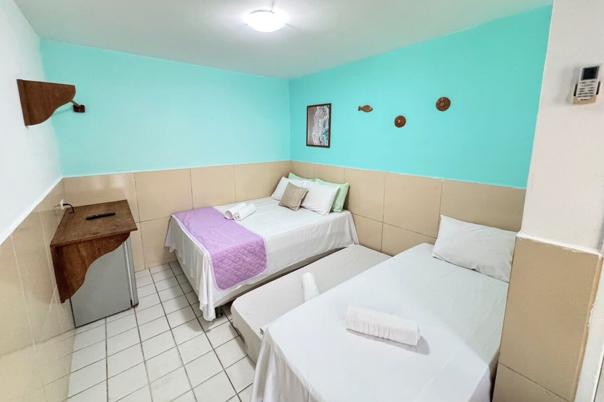 A hotel room with two beds, a small wooden side table, a wall-mounted telephone, and a ceiling light.