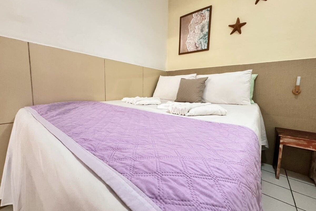 A hotel room with a bed, pillows, a blanket, a wall with a painting, and a star decoration.