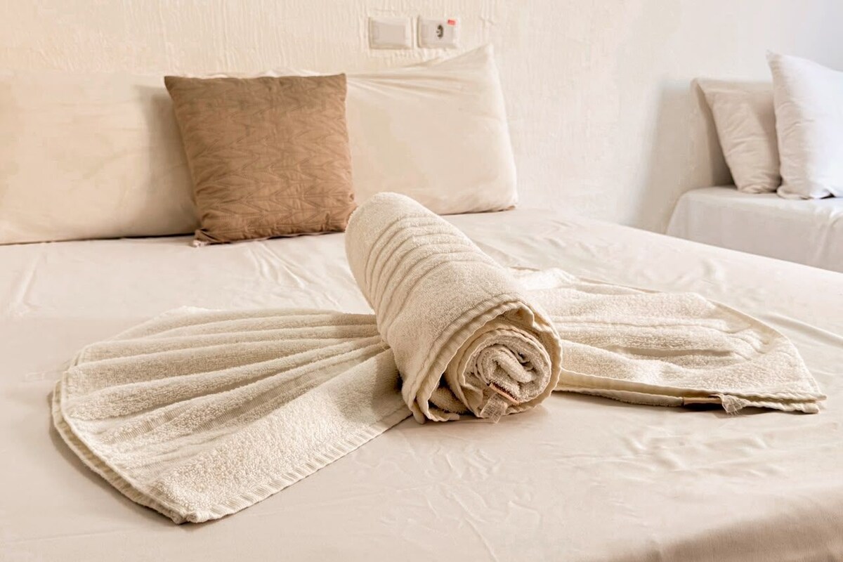 A neatly made bed with a rolled towel and a folded towel on a white bedspread.
