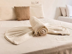 A neatly made bed with a rolled towel and a folded towel on a white bedspread. - Pousada Boas ondas (Ipojuca)