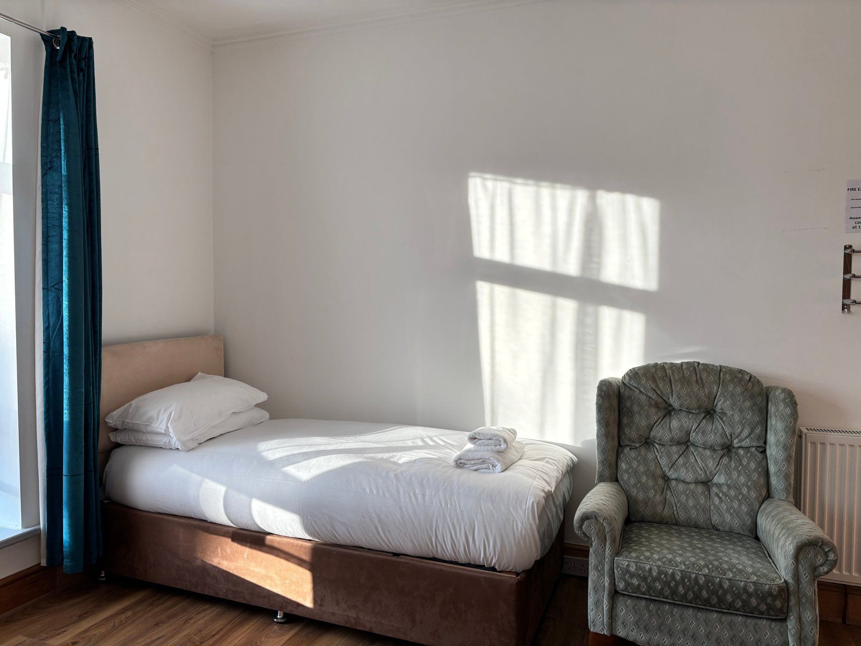 A single bed with a headboard, a chair, and a window with curtains.