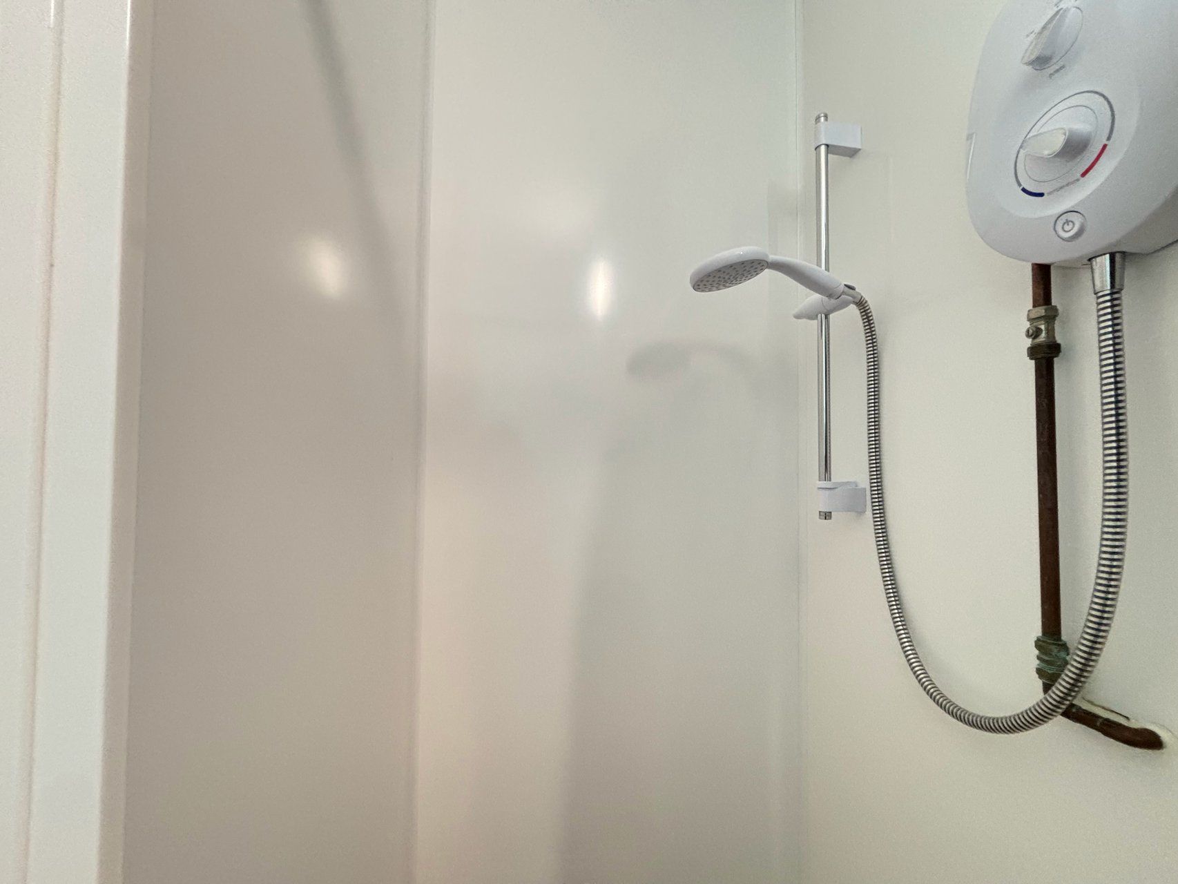 A shower with a handheld showerhead and a wall-mounted control panel.