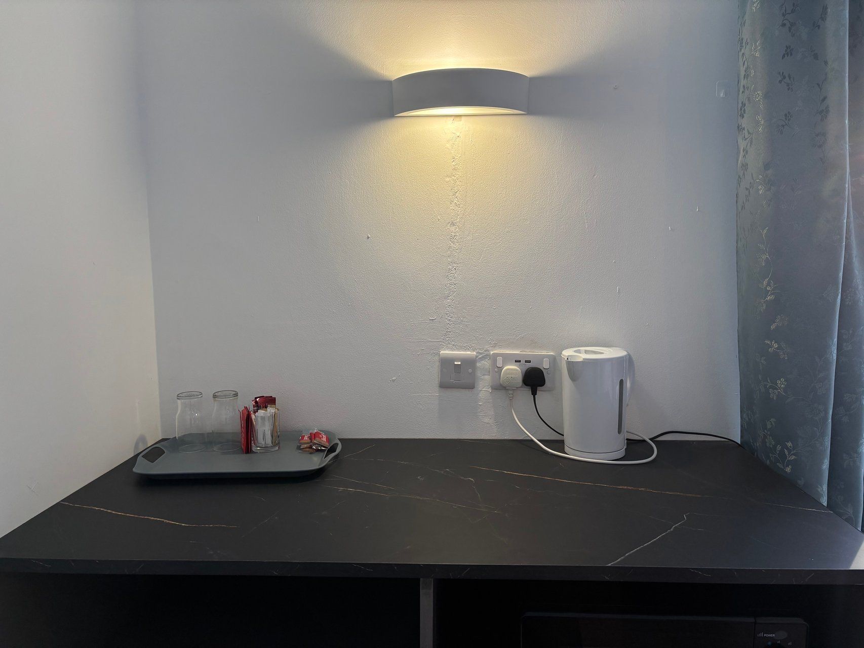 A room with a black marble table, a wall-mounted light, and a power outlet with a plug.