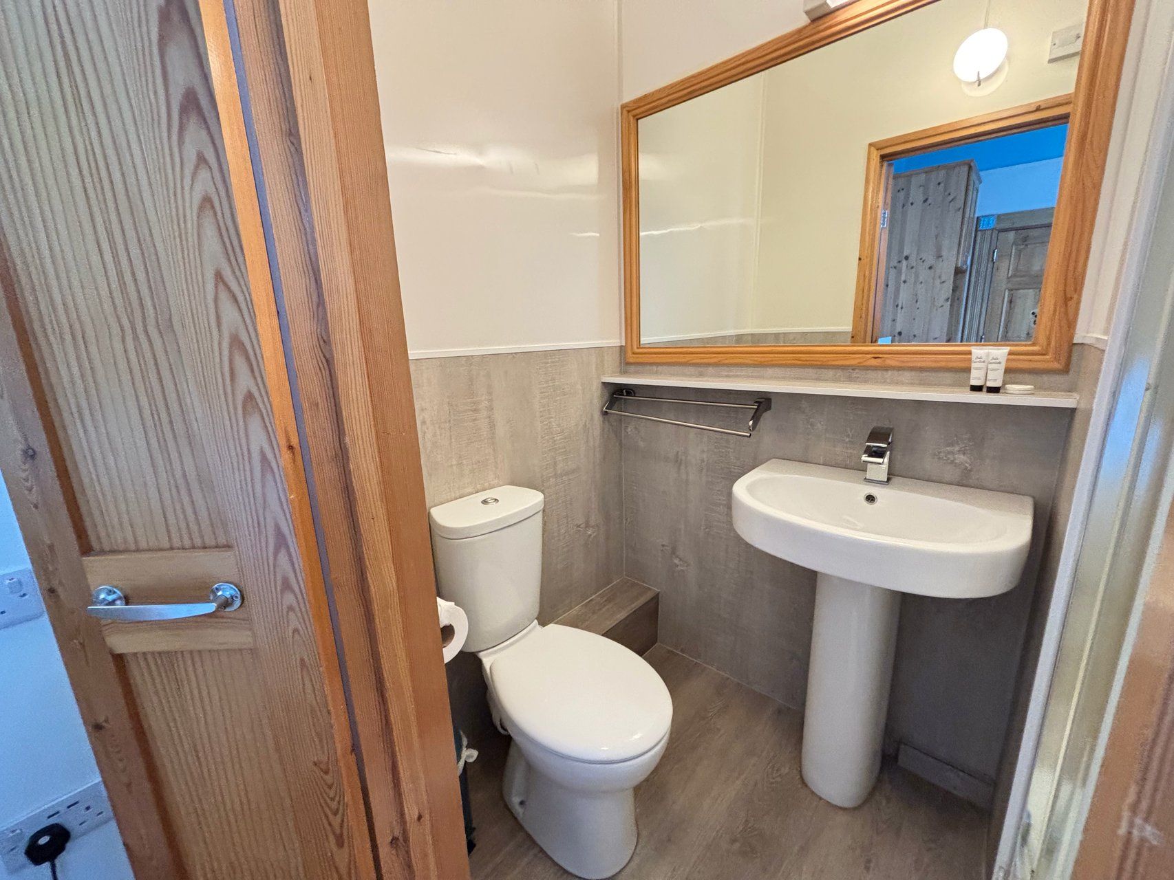 Un baño peque ño con inodoro, lavamanos y puerta de madera.