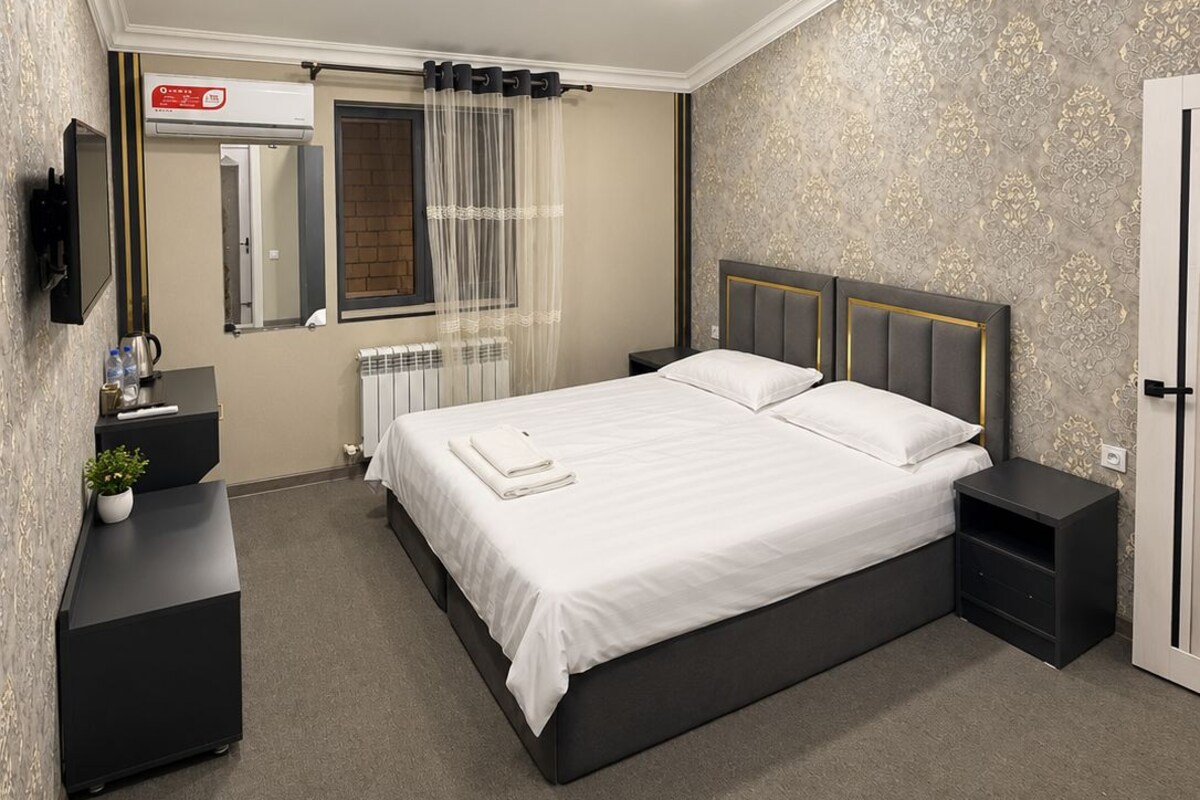 A bedroom with a bed, bedside tables, a TV, a radiator, and a mirror.