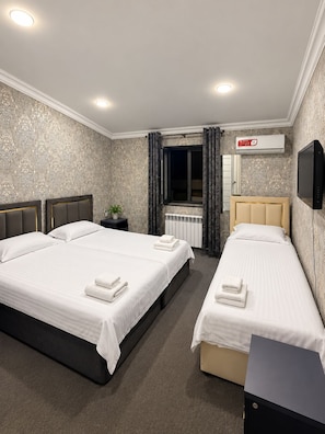 A hotel room with two beds, a television, an air conditioning unit, and a window with curtains. - The Lotus Hotel (Tashkent)
