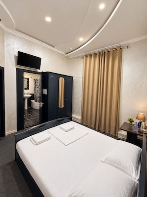 A hotel room with a bed, a desk with a lamp, a TV, and a bathroom visible through an open door. - The Lotus Hotel (Tashkent)