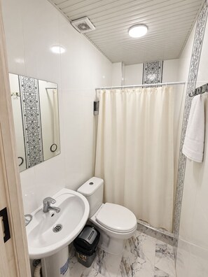 A bathroom with a white sink, toilet, and shower curtain. - The Lotus Hotel (Tashkent)