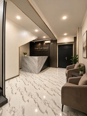 A reception area with a marble reception desk, a black door, and a seating area with two sofas. - The Lotus Hotel (Tashkent)