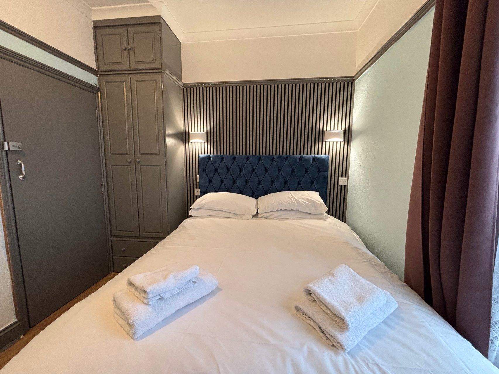 Una habitación de hotel con cama, armario y cabecera con líneas verticales.