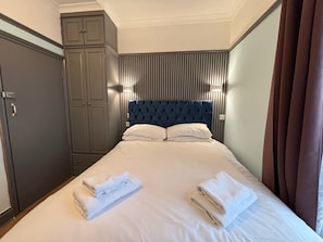 Una habitación de hotel con cama, armario y cabecera con líneas verticales.