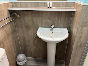 Un baño con un lavamanos blanco, un perchero y un pequeño cubo de basura.