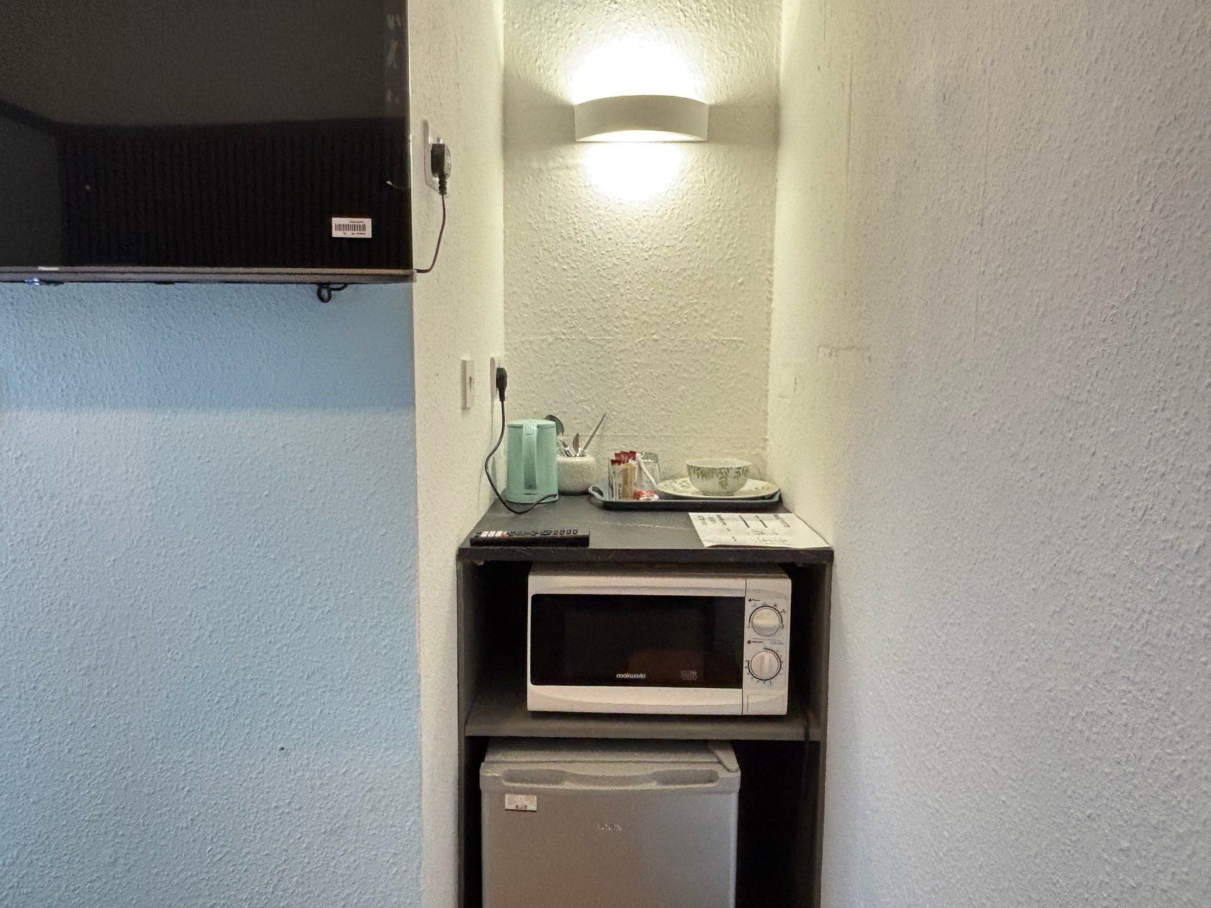 Una kitchenette compacta con microondas, un refrigerador pequeño y una lámpara sobre la encimera.