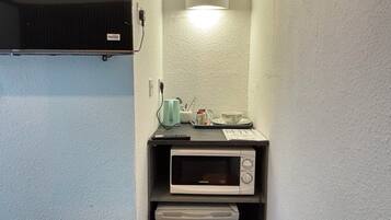 Una kitchenette compacta con microondas, un refrigerador pequeño y una lámpara sobre la encimera.