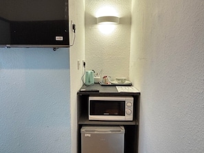 Una kitchenette compacta con microondas, un refrigerador pequeño y una lámpara sobre la encimera.