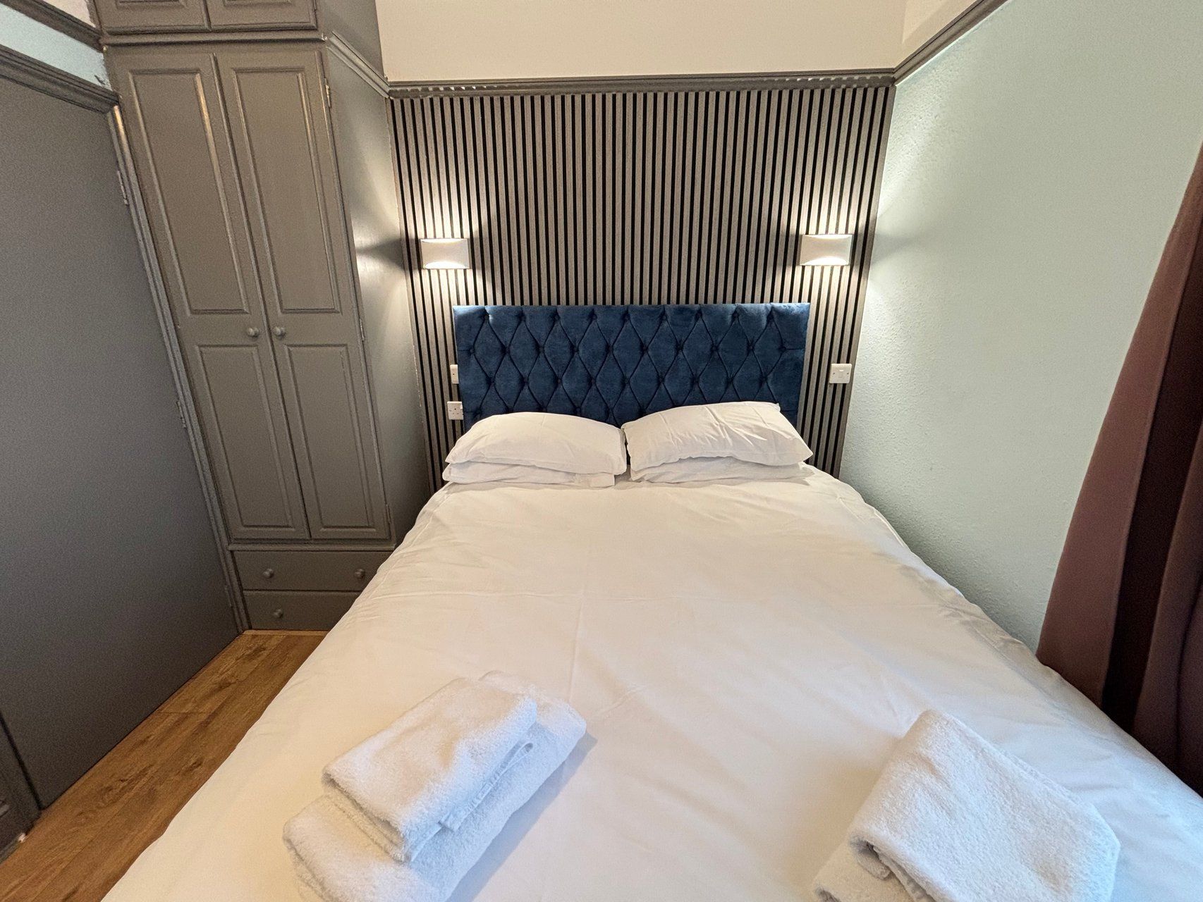 Una habitación de hotel con cama, armario y cabecera con líneas verticales.