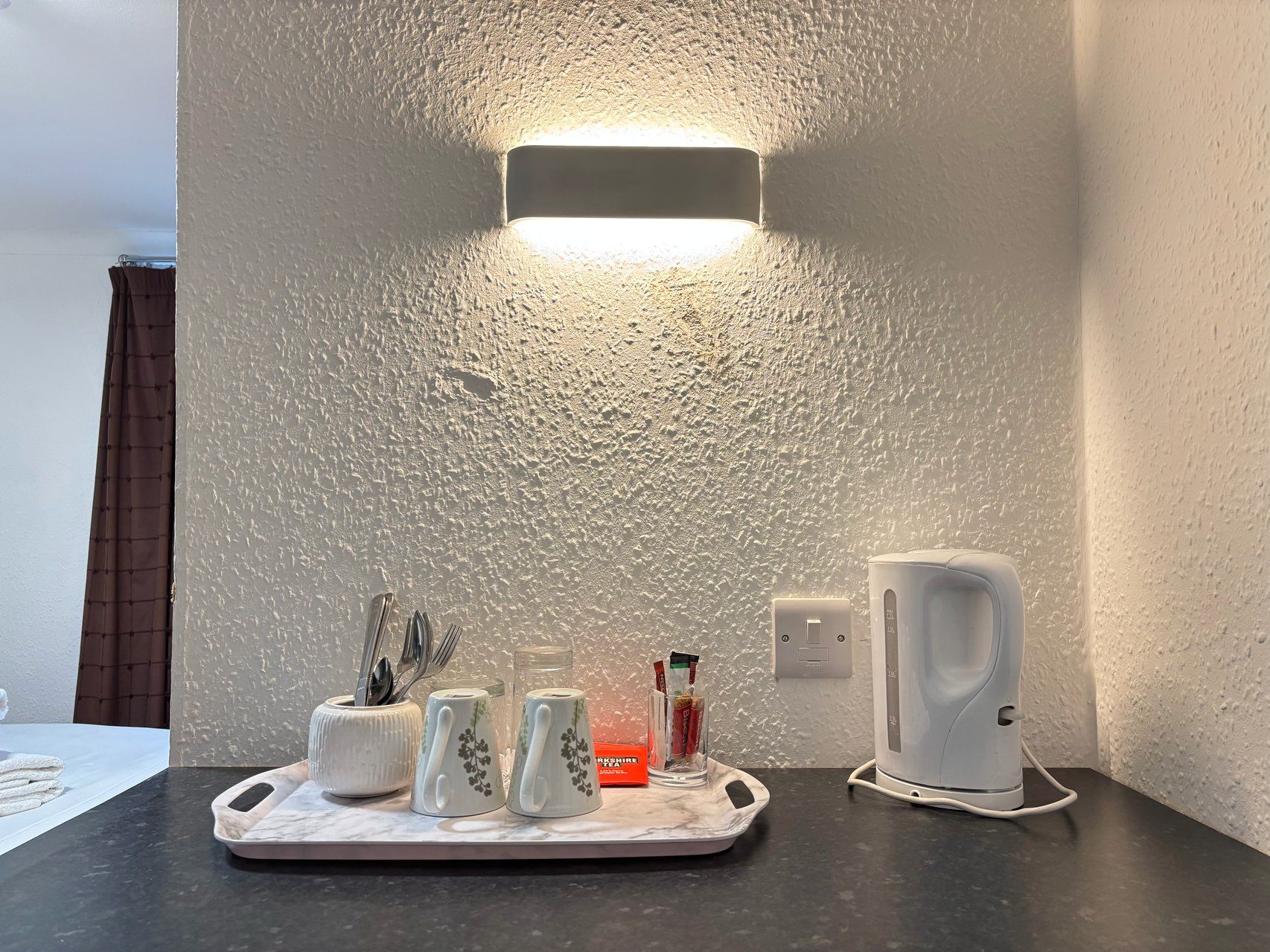 Una encimera de cocina con una bandeja que contiene tazas, una tetera y un vaso con condimentos.