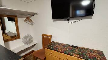 A bedroom with a bed, a dresser, a mirror, a television mounted on the wall, and a fan on the floor.