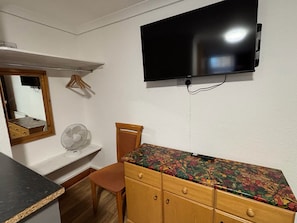 Un dormitorio con cama, cómoda, espejo, televisor montado en la pared y un ventilador en el suelo.