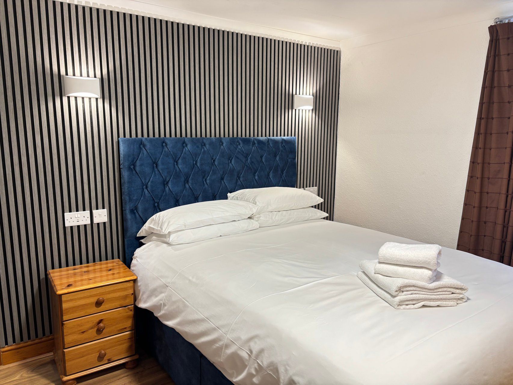 Una habitación de hotel con una cama, una mesita de noche de madera y una pared con listones verticales.