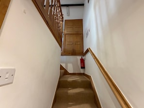 Una escalera estrecha con peldaños alfombrados que conduce a una puerta de madera.