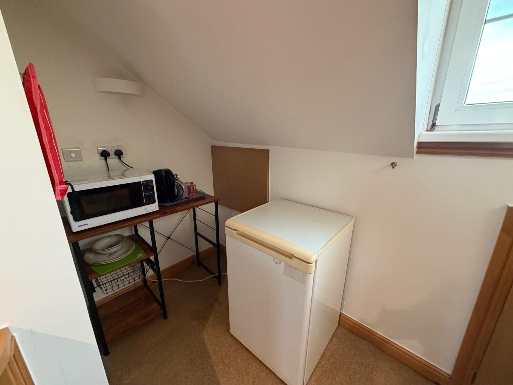 Una kitchenette compacta equipada con microondas, cafetera y refrigerador pequeño.