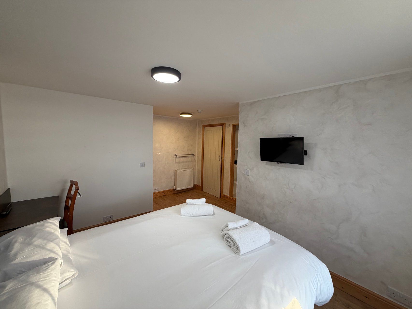 Habitación de hotel con cama, televisión montada en la pared y suelo de madera.