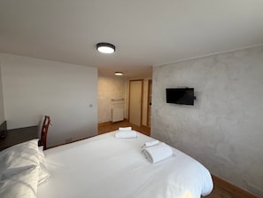 Habitación de hotel con cama, televisión montada en la pared y suelo de madera.