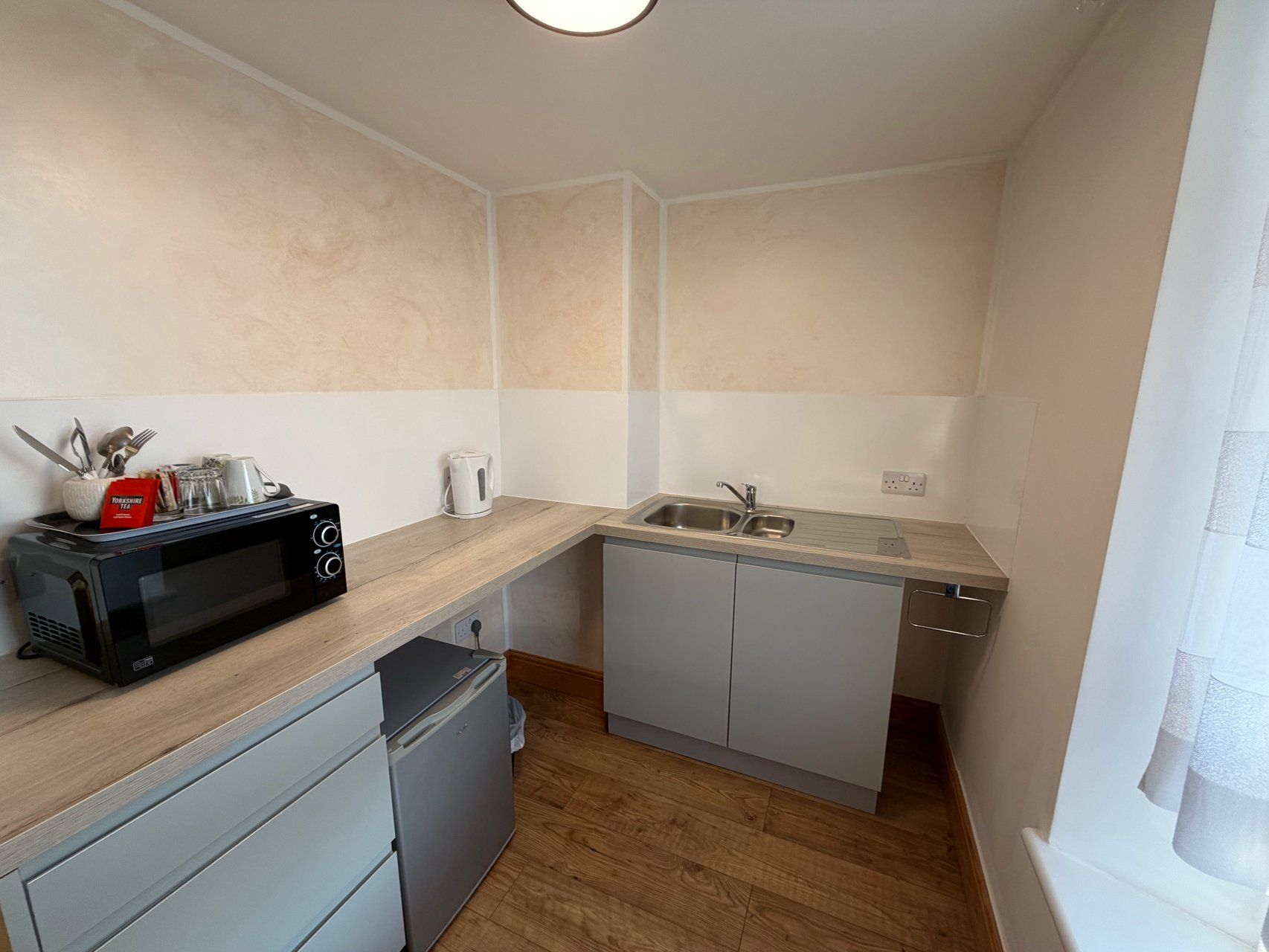 Cocina pequeña con microondas, hervidor y lavabo.