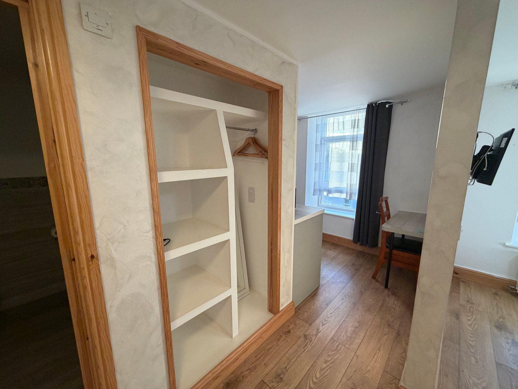 A room with a wooden wardrobe, a window with curtains, and a chair.