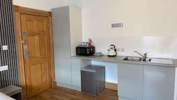 A compact kitchen with a microwave, kettle, and sink.