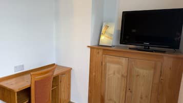 Quarto com escrivaninha de madeira, uma cadeira, televisão em um armário de madeira e uma tomada na parede.