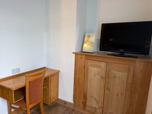 Een kamer met een houten bureau, een stoel, een televisie op een houten kast en een stopcontact.