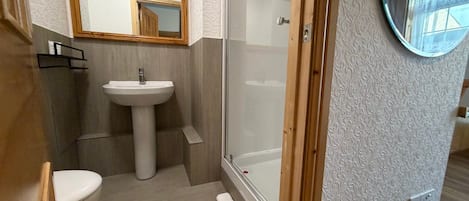 Un baño con lavamanos pedestal, inodoro, cabina de ducha y espejo.