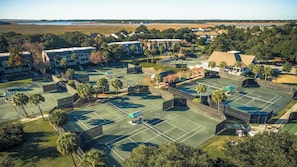 An aerial view of a resort with multiple tennis courts, surrounded by buildings and palm trees.