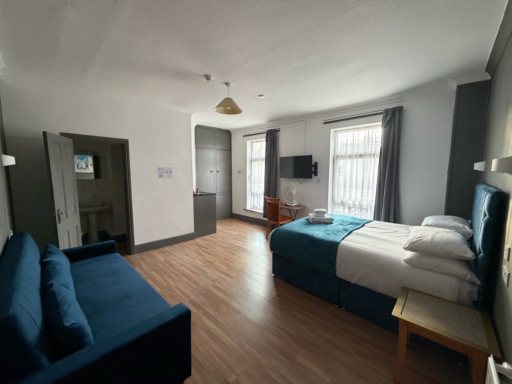 A hotel room with a bed, a desk, a chair, a sofa, and a television.