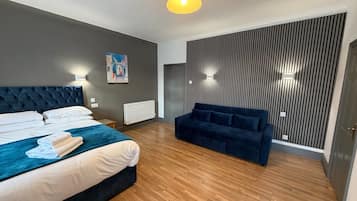 A hotel room with a bed, a sofa, a radiator, a painting, and a wall with vertical lines.