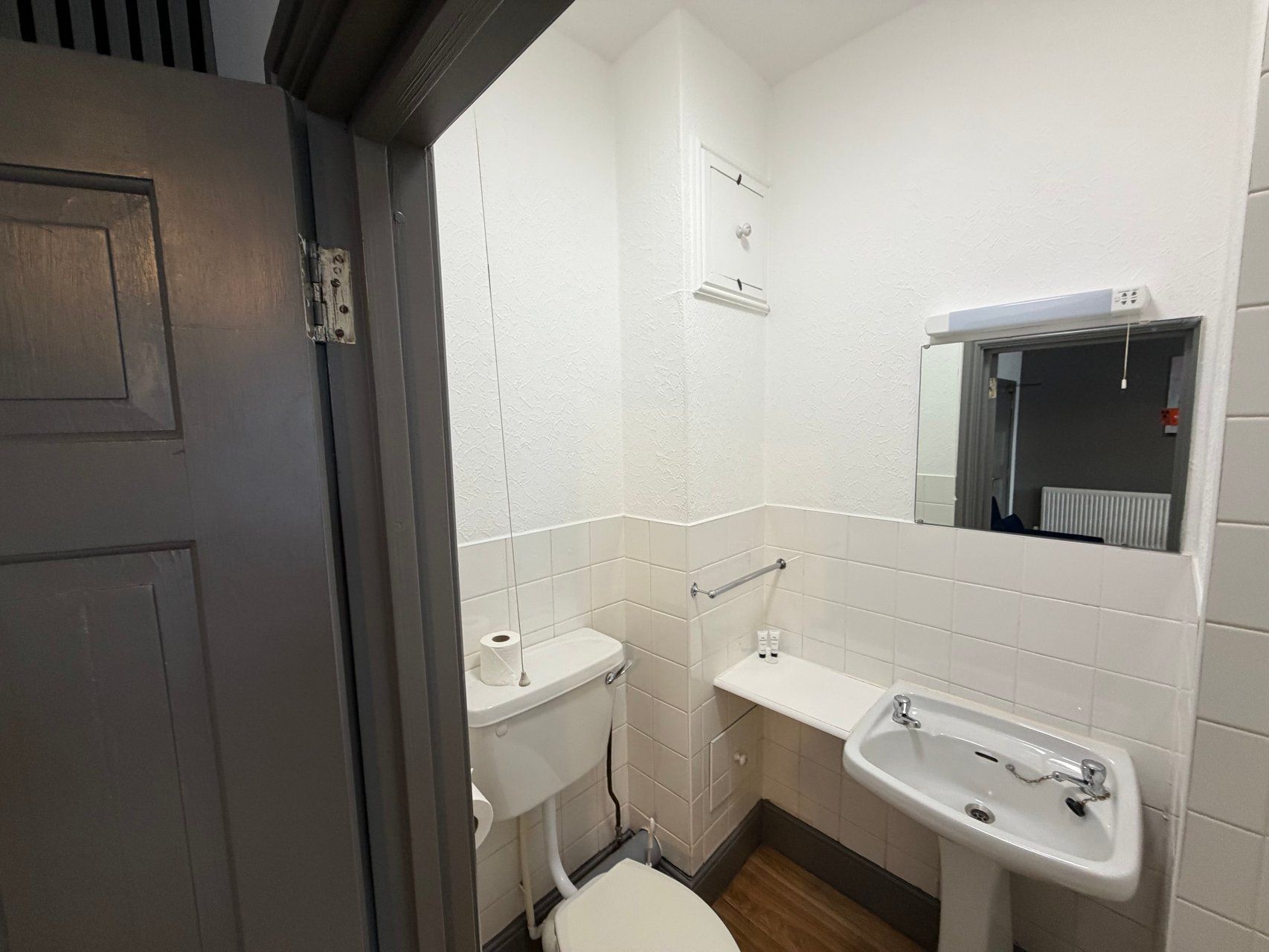 Een kleine, praktische badkamer met toilet, wastafel en spiegel.