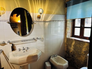 Ein Badezimmer mit einem weißen Waschbecken, einem Spiegel, einem Bidet und einem Fenster mit Blick auf Gebäude.
